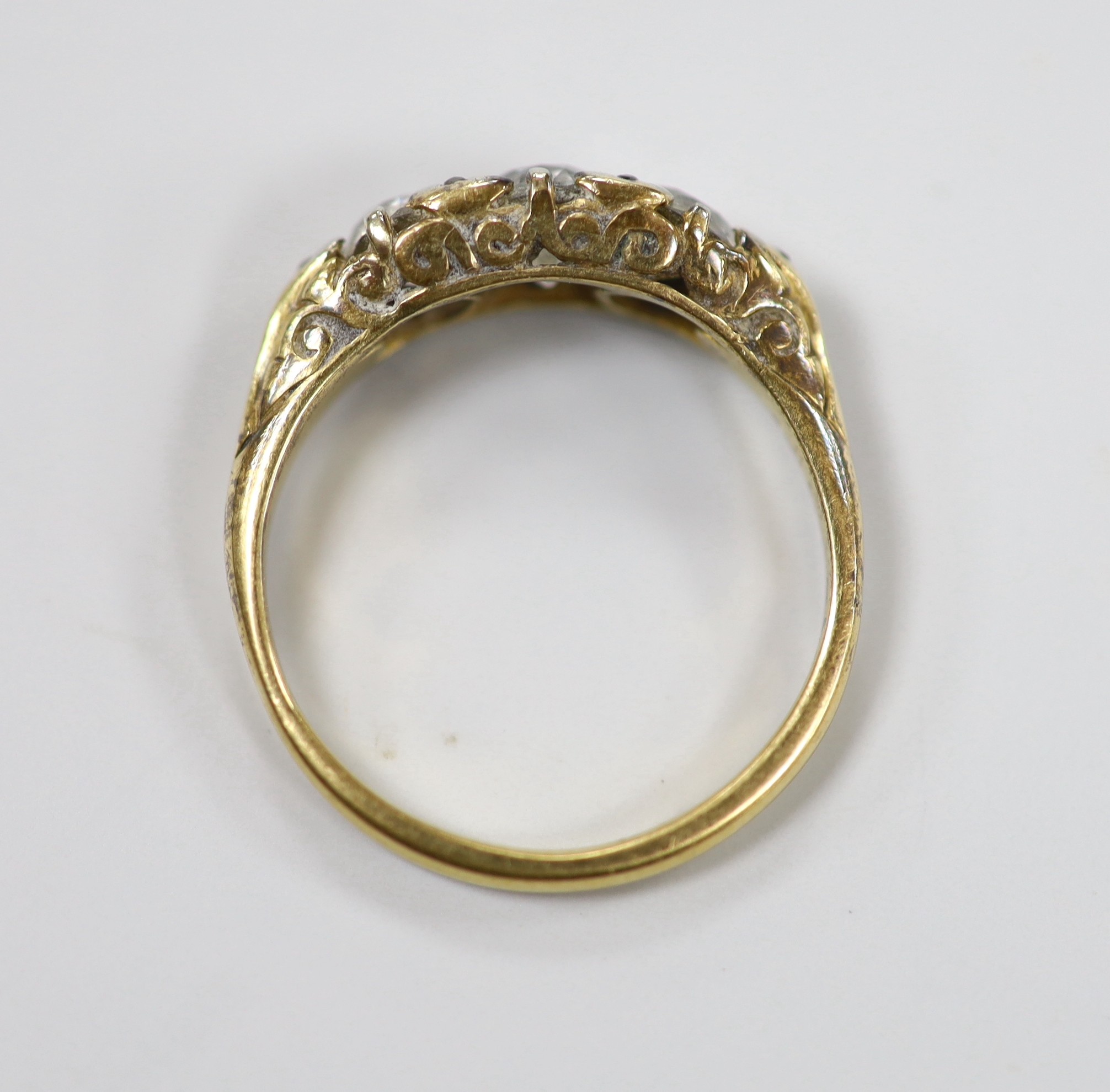 An antique yellow metal and graduated three stone diamond set ring, with diamond chip set spacers, size N/O, gross weight 4 grams